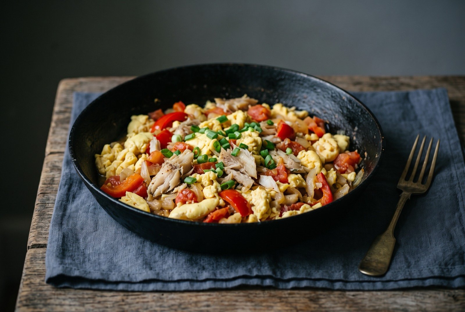 Ackee and saltfish: soft pale yellow ackee folded through flaked white saltfish with red pepper and tomato, no egg present despite the resemblance, the tinned ackee version a Windrush household actually cooked.