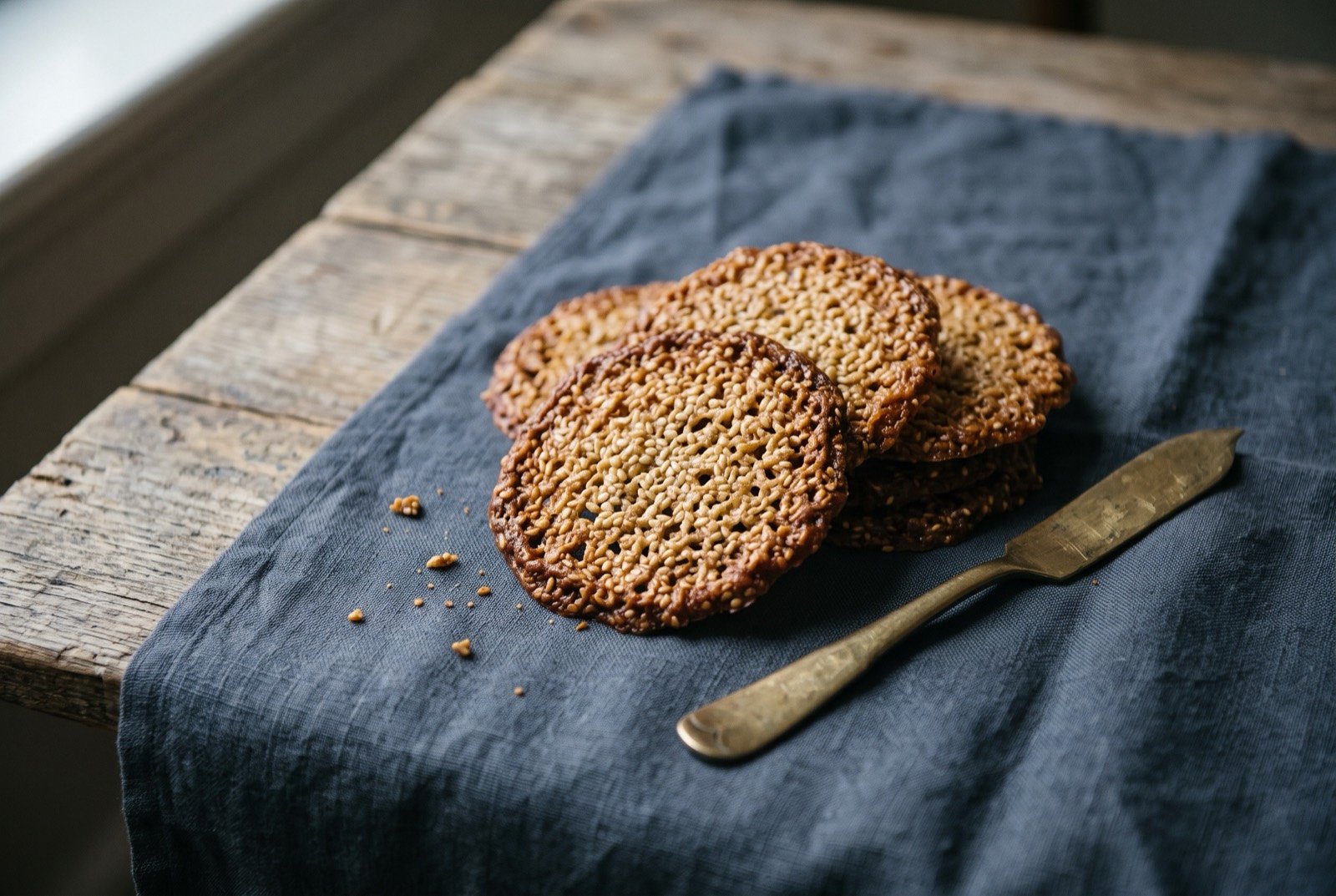 Benne wafers, thin lacy sesame seed cookies: a small loose pile of thin, flat, deeply golden brown wafers, their edges lacy and slightly darker than the centres, dense with visible toasted sesame seed across every wafer.