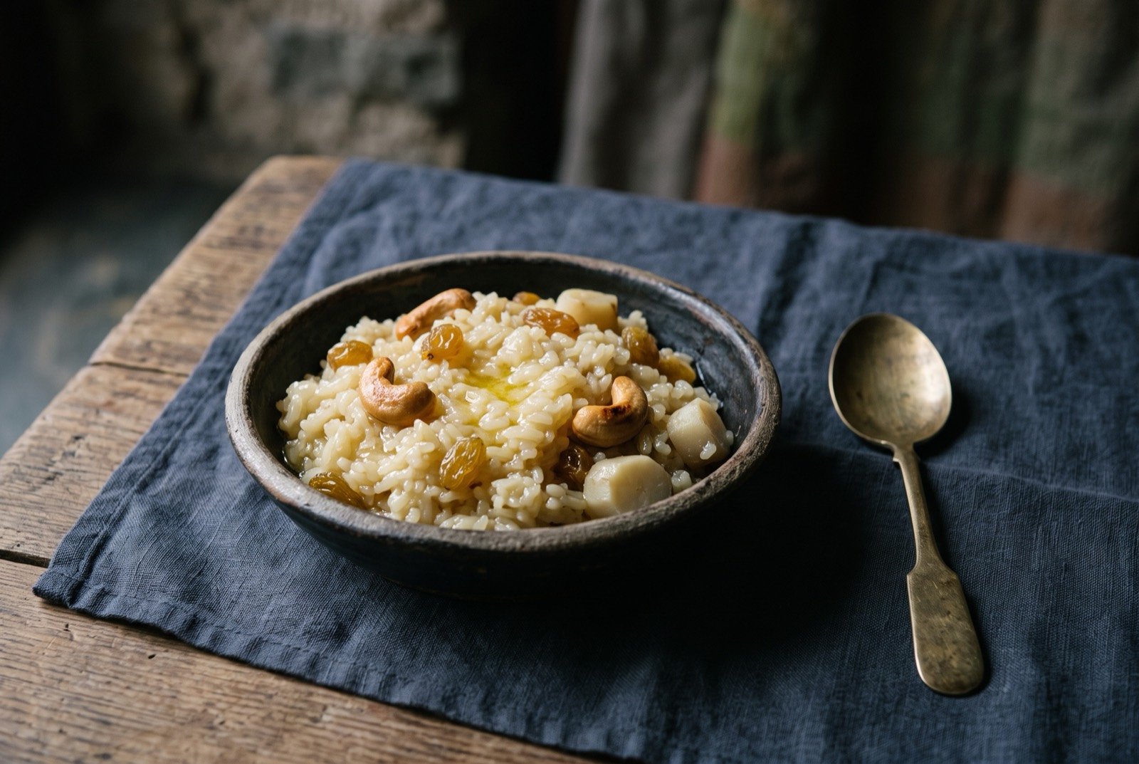 Dresi, festival sweet rice with yak butter, cashews and raisins: a small bowl of glossy pale rice studded with golden raisins and whole cashews, a few pieces of pale wild droma tuber visible among the grains.