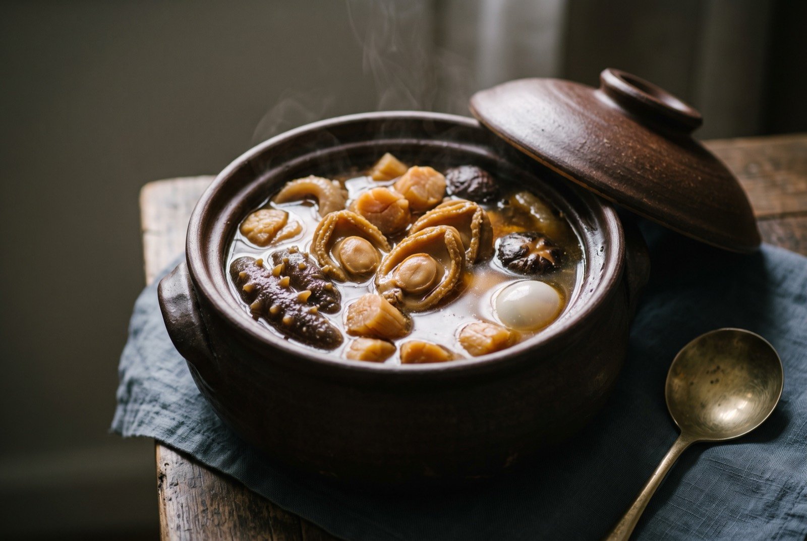 Fotiaoqiang, Buddha Jumps Over the Wall, sealed in its earthenware jar: a squat, rounded earthenware jar with its domed lid lifted and resting beside it, releasing steam, the jar packed to the rim with a rich dark amber broth crowded with whole abalone.