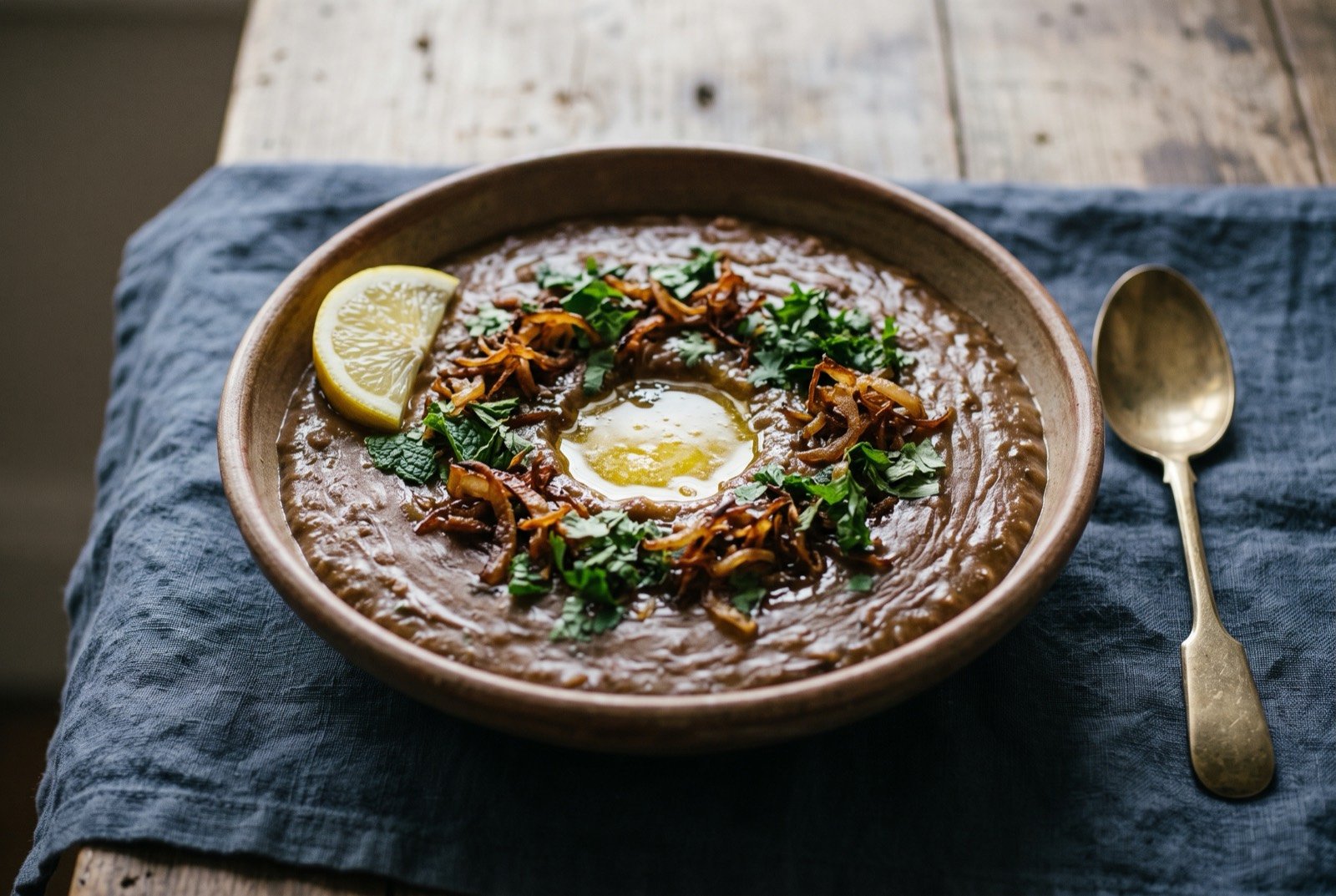 Hyderabadi haleem, wheat and meat pounded for hours into a single smooth paste: a wide shallow bowl of thick, dense, dark brown porridge with a smooth, faintly fibrous sheen, a pool of golden ghee melted into a small well at the centre.