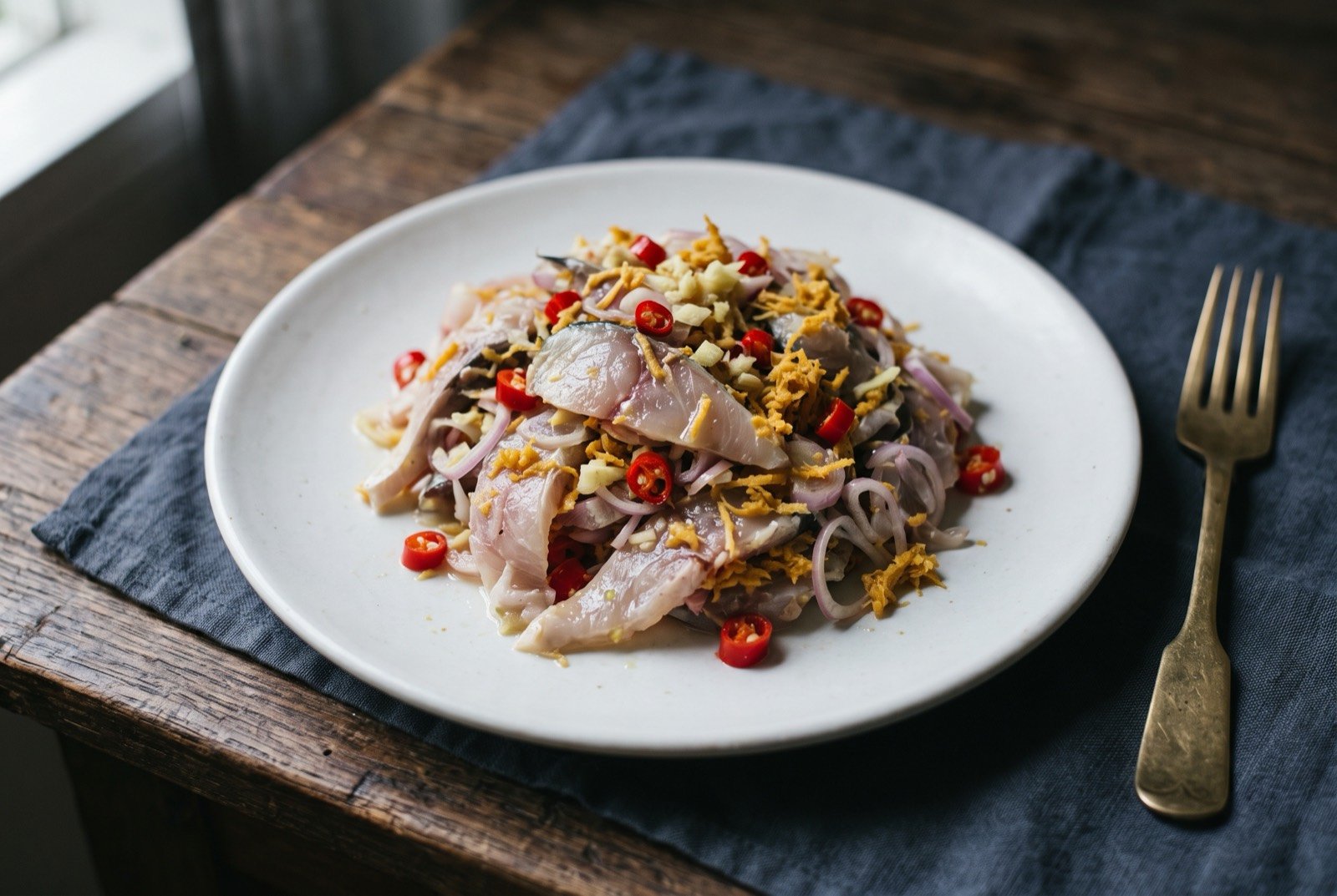 Hinava, Kadazan-Dusun raw fish with bambangan: thin slices of pale raw mackerel tossed with shallot, ginger and red chilli, a scattering of coarse grated ochre-coloured bambangan kernel through it.