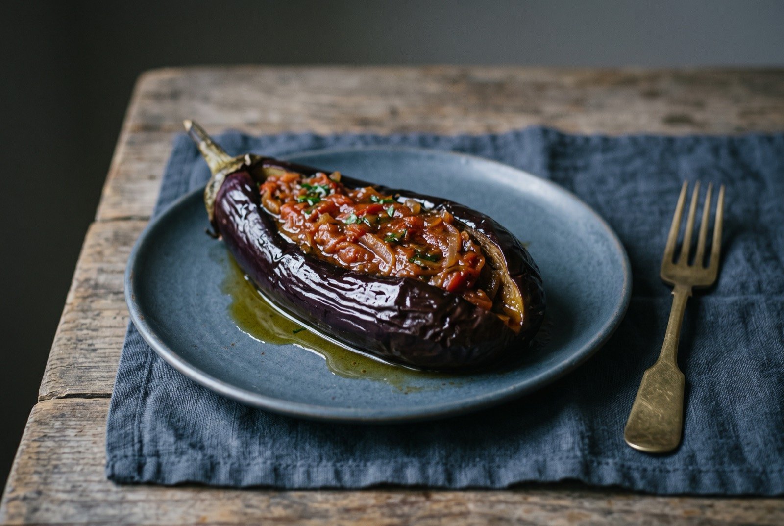 Imam bayıldı, whole aubergine braised in olive oil with onion and tomato: a whole deep purple aubergine, split lengthways and collapsed soft, its slit filled with a glossy reduced onion and tomato mixture.