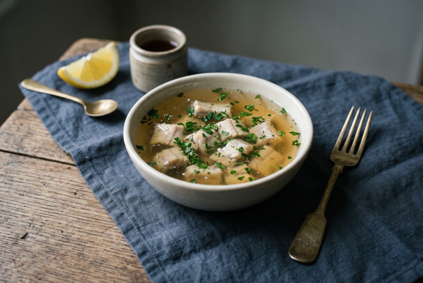 Jellied eels, cold set eel in its own stock: chunks of pale eel suspended within a clear, faintly amber, wobbling jelly in a small white bowl, a scatter of chopped parsley visible within the set.
