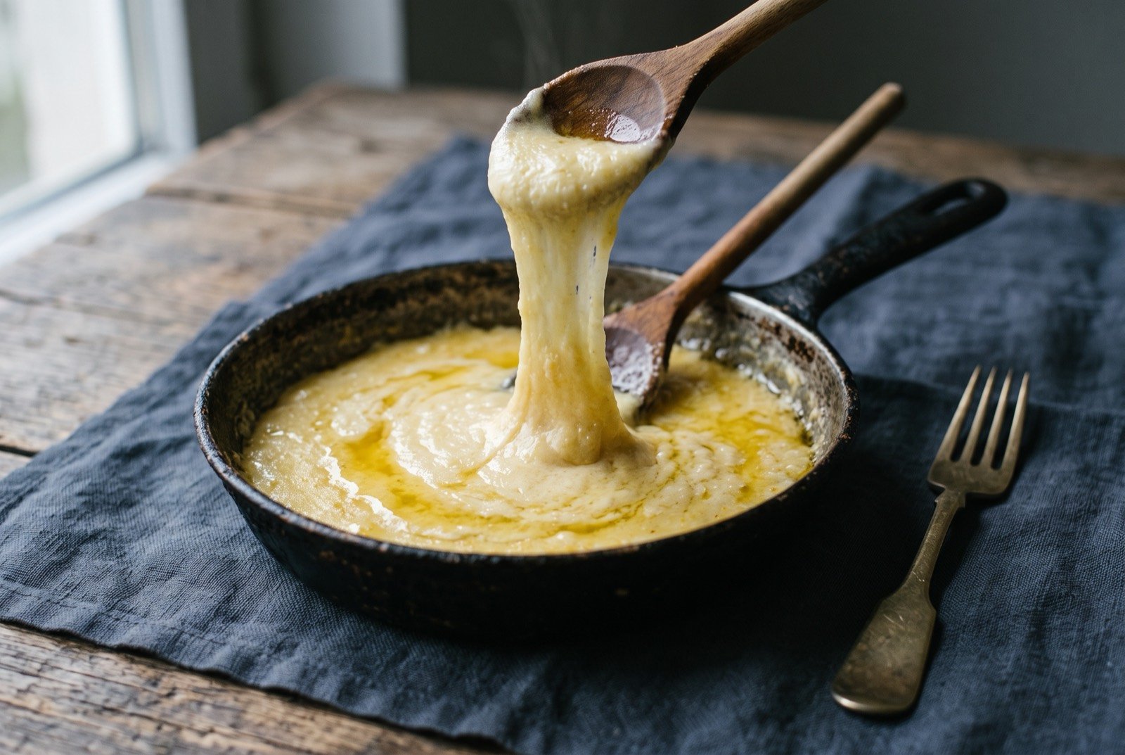 Kuymak, cornmeal and cheese worked together until molten and elastic: a small blackened pan of pale golden cornmeal porridge, a distinct glossy layer of butter fat pooling and separating on its surface.