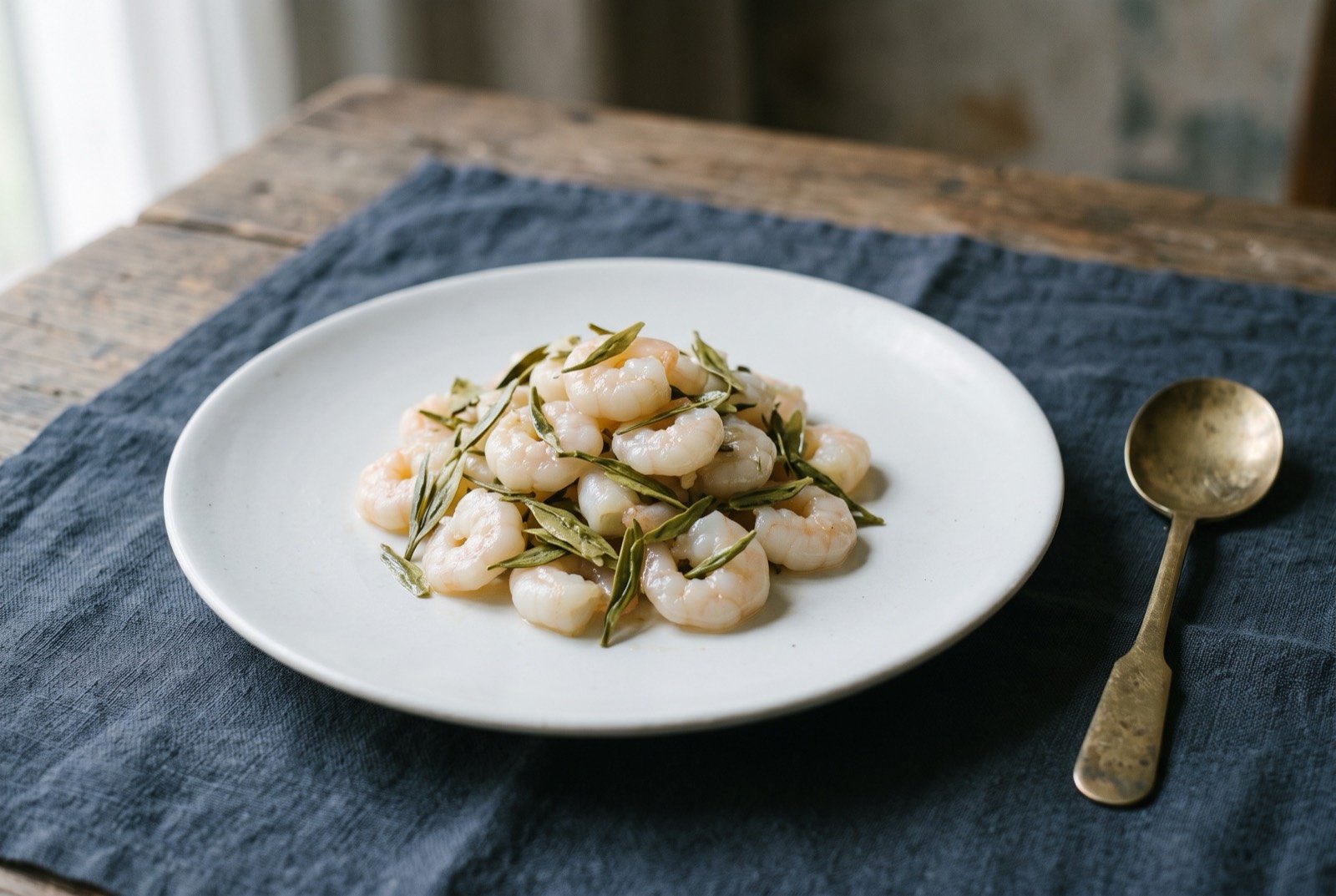 Longjing xiaren, small river shrimp tossed through brewed green tea: a small mound of jade-white shrimp scattered with whole pale green tea leaves, a faint translucent sheen across the shrimp rather than a heavy sauce.