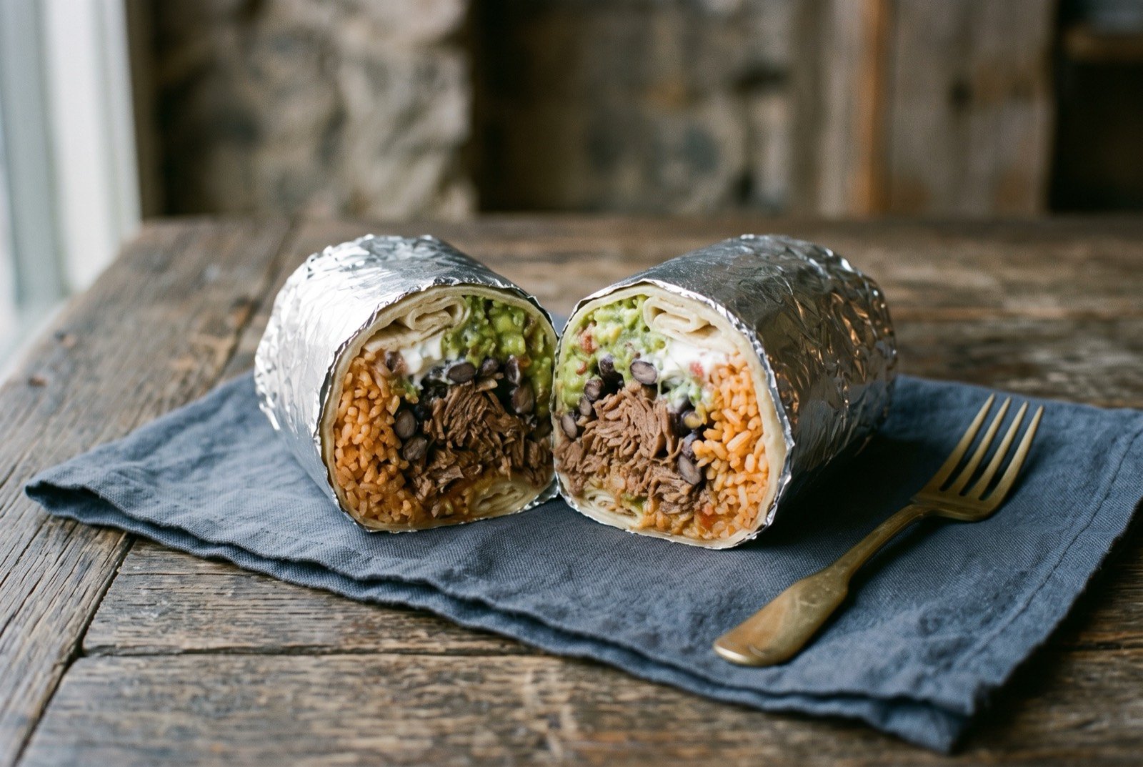 The Mission burrito: a large foil wrapped burrito, the foil peeled back at one end to reveal a thick cross section of orange rice, dark beans.