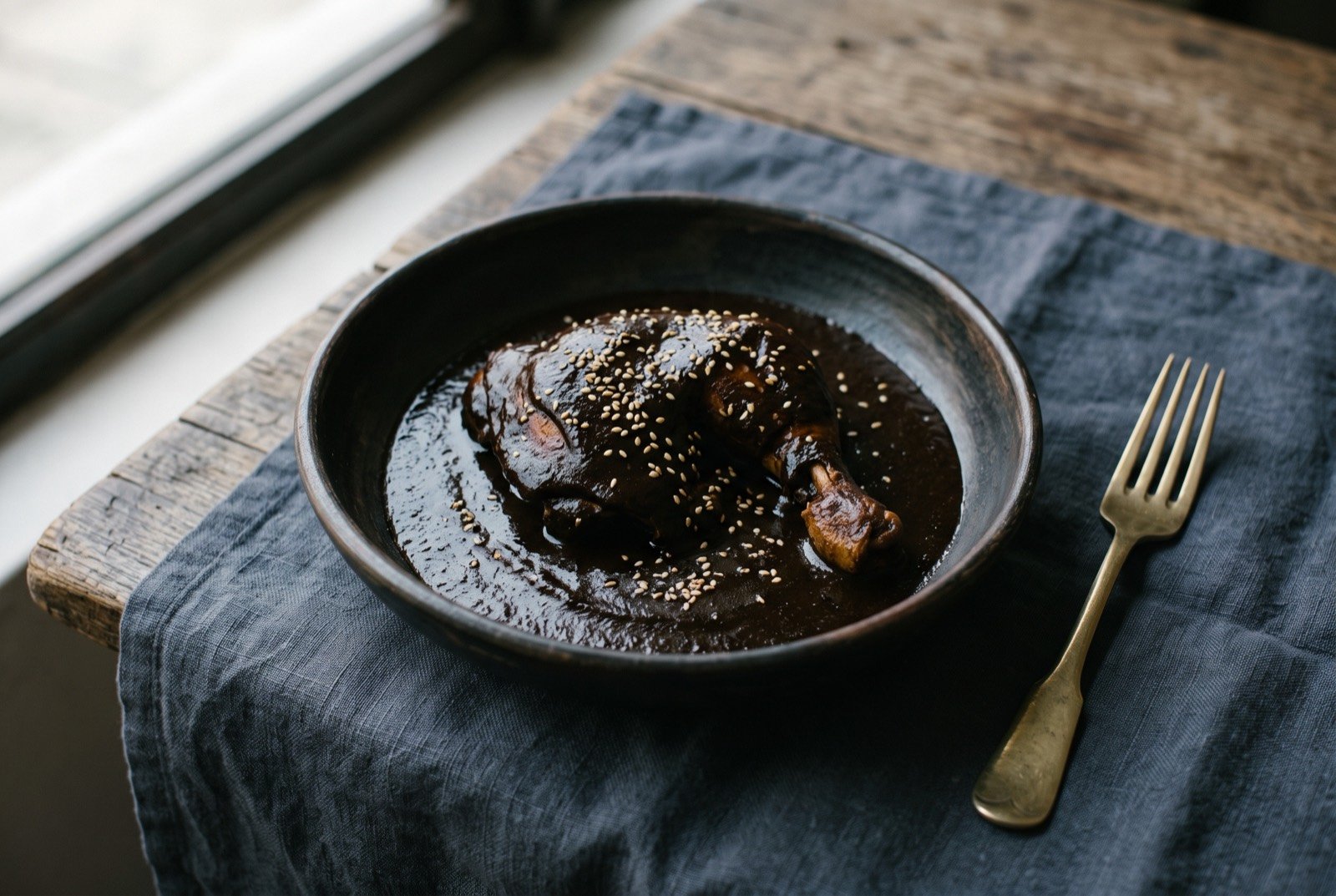 Mole negro oaxaqueño, Oaxaca's near black chile and chocolate mole: an almost black, dense, glossy sauce pooled generously around a piece of braised chicken, the deep near obsidian colour catching the light in a faint sheen.