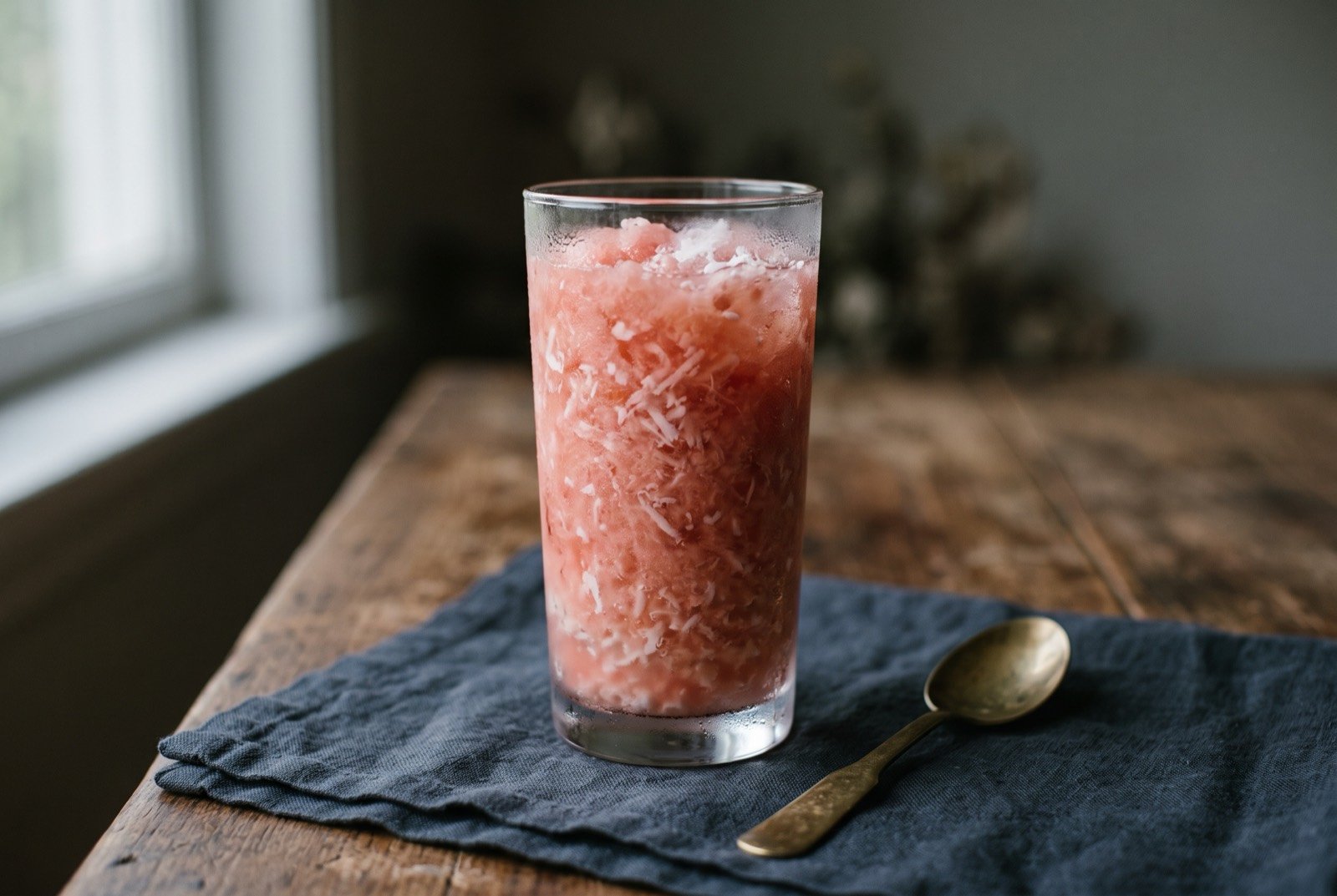 ʻotai, Tongan watermelon and coconut drink: a tall glass filled with pale pink, finely crushed watermelon and coconut, flecks of white coconut flesh suspended through it.