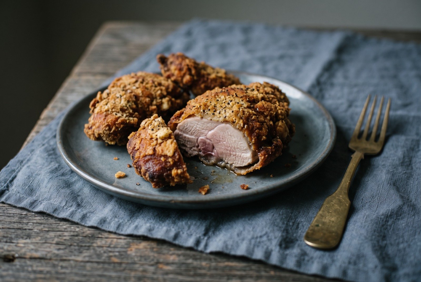 Pan-fried ptarmigan in a cracker crust: golden brown, deeply crisped pieces of pan-fried game bird in a coarse cracker crust, arranged on a plate with a wedge cut away to show pale.