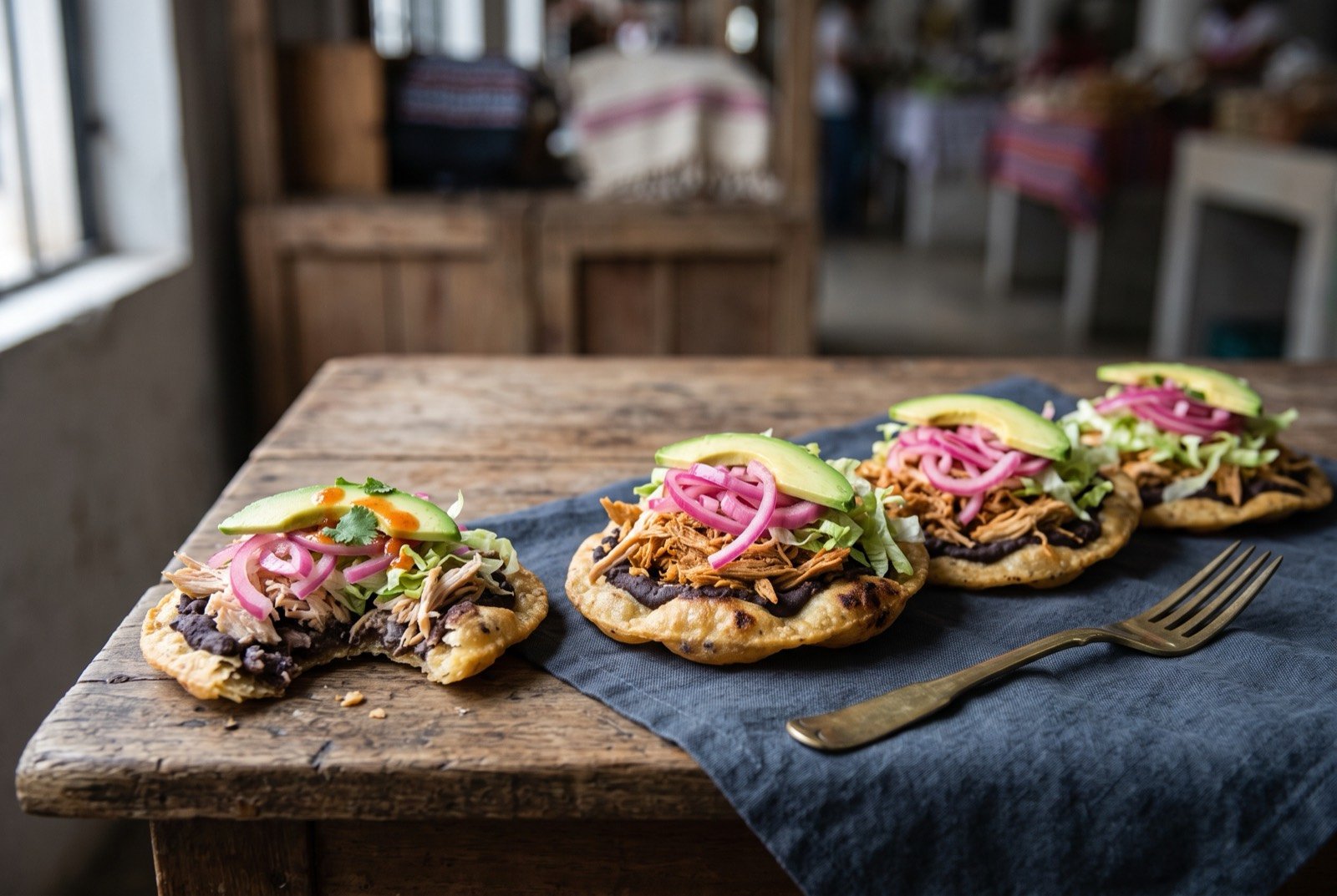 Panuchos, fried bean stuffed tortillas with shredded turkey: a row of small round fried tortillas with a puffed, blistered edge, one broken open to show a dark bean filling pressed inside.