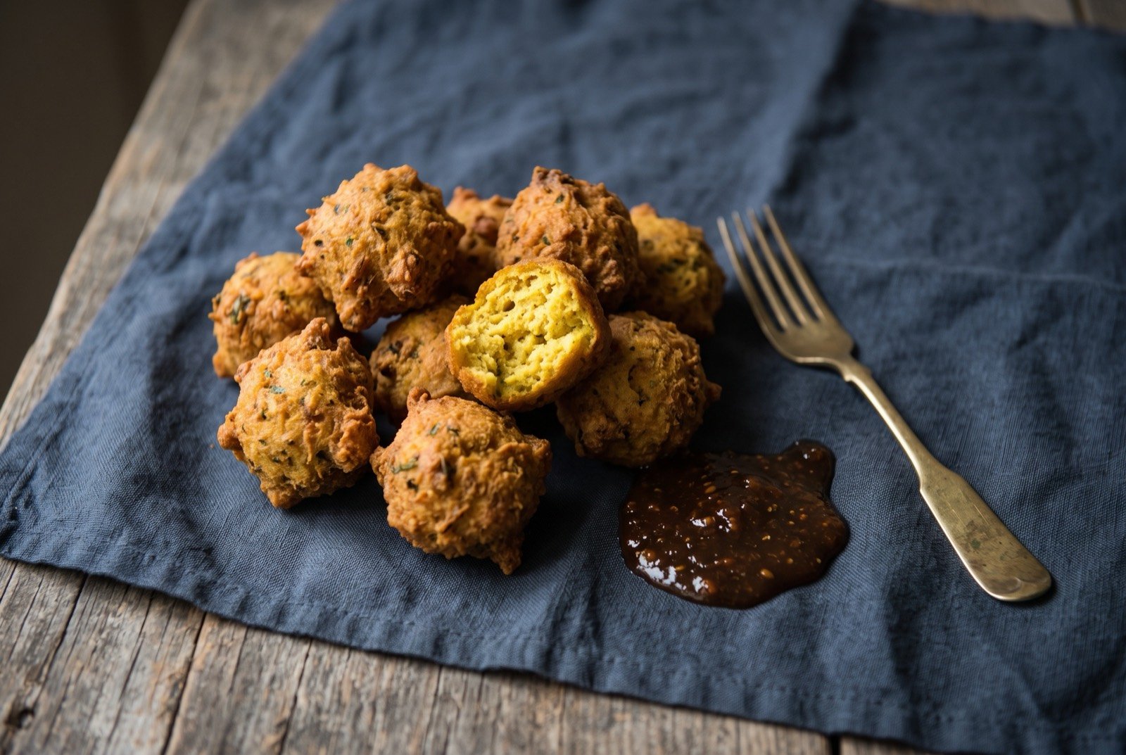 Pholourie, spiced split pea fritter balls: a small pile of golden brown, irregularly round fried fritters with a rough, craggy surface, one broken open to show a soft yellow interior.