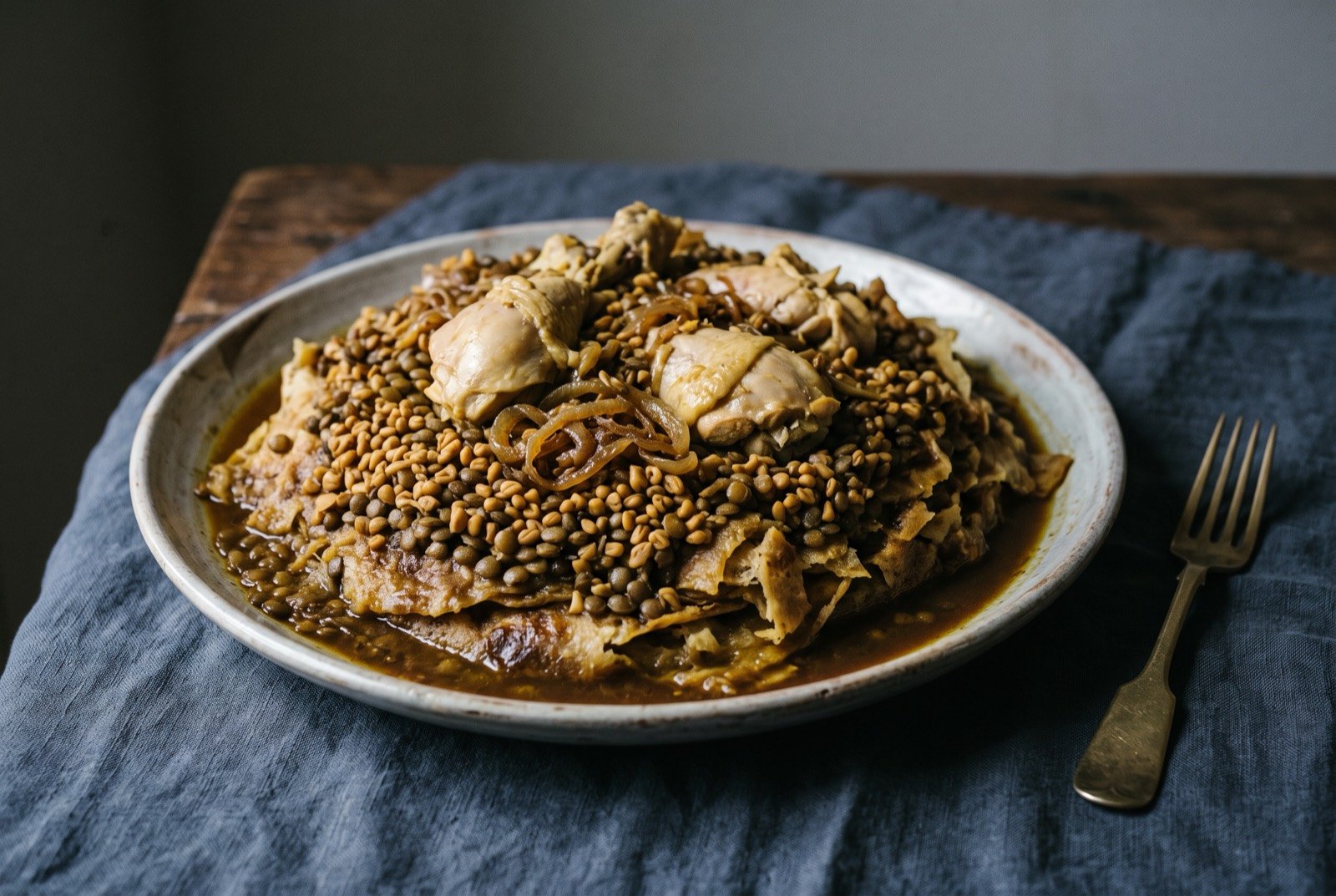 Rfissa: A wide platter of torn laminated flatbread soaked dark with saffron and ginger broth, mounded with lentils and swollen fenugreek seeds.