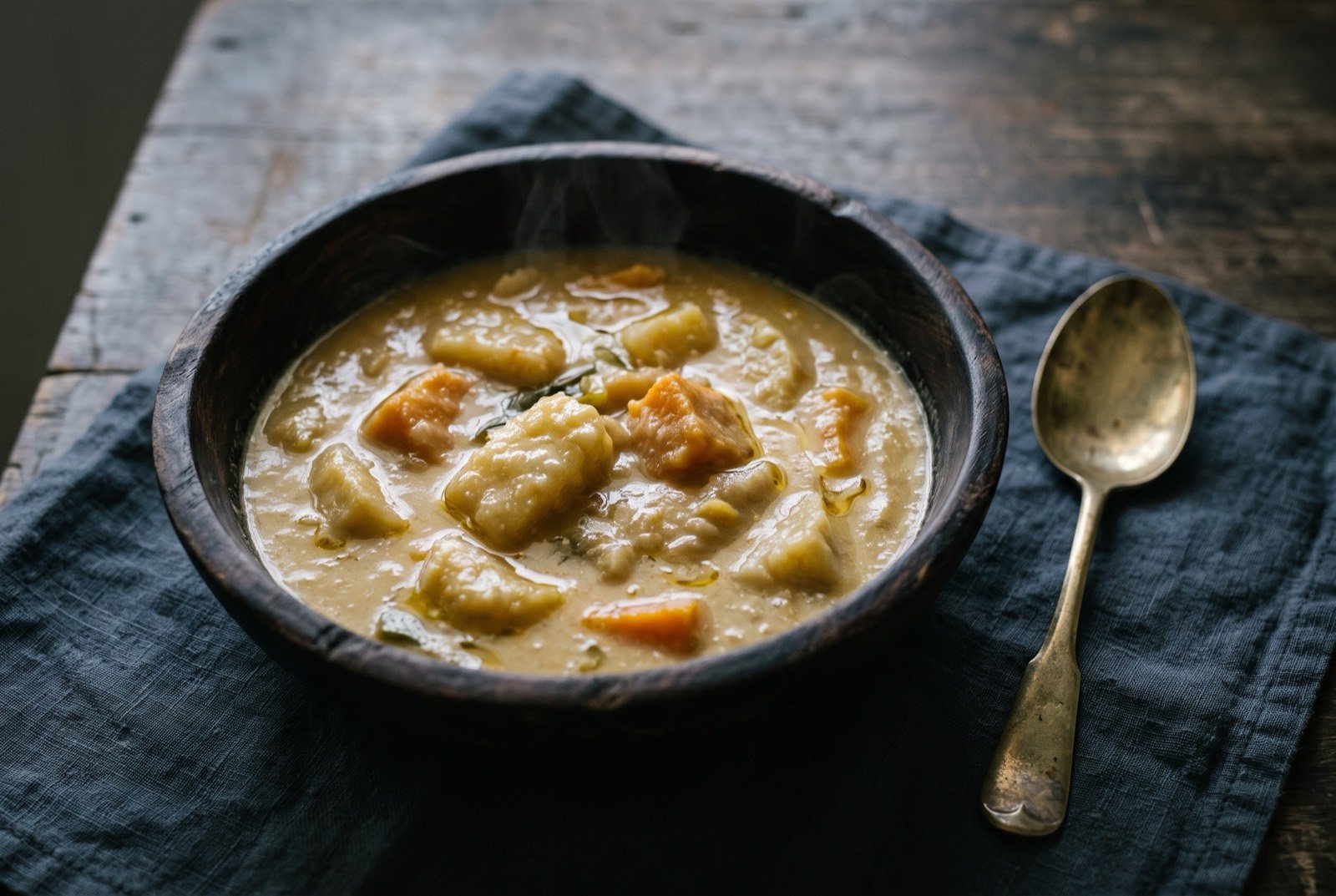 Sop sop, a Torres Strait yam stew: a thick, pale golden stew of tender yam pieces in a glossy coconut sauce, served in a dark wooden bowl, a faint sheen of oil pooling at the surface.