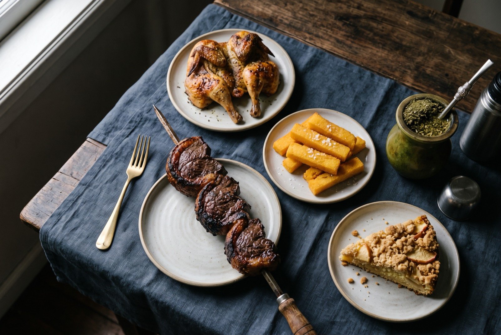 The Gaúcho South table: a wide dark wooden table seen from above, a skewer of charred coarse salted beef beside a rounded green cuia gourd with its metal bombilla.